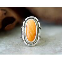 Oval orange spiny oyster cabochon in a bezel setting accented with stamped cutout wire on a wide silver band that is tapered and oxidized 6
